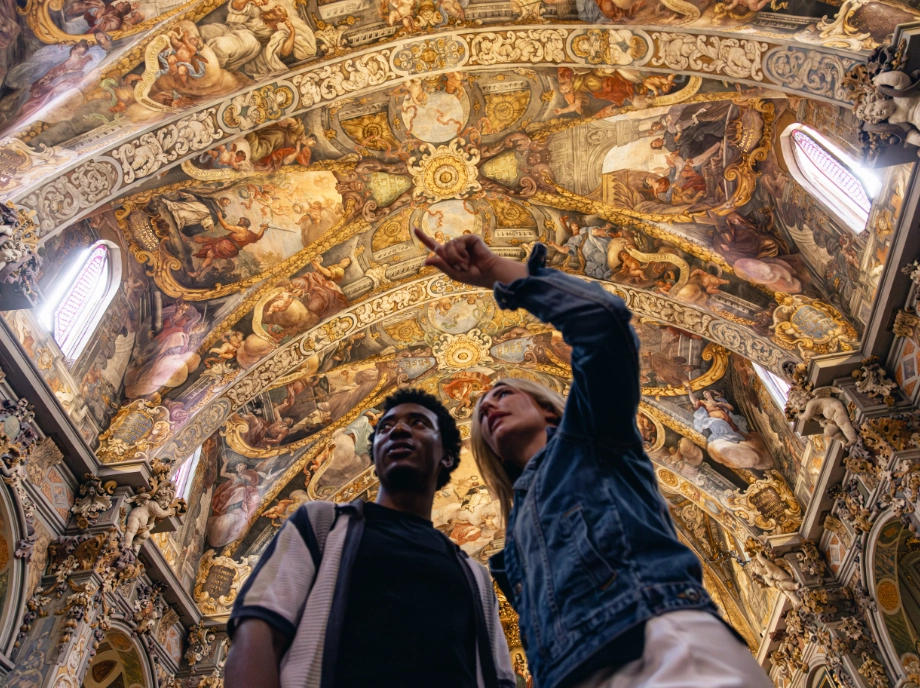Dos visitantes contemplando el techo decorado de una iglesia histórica durante un tour de arte y arquitectura en Valencia
